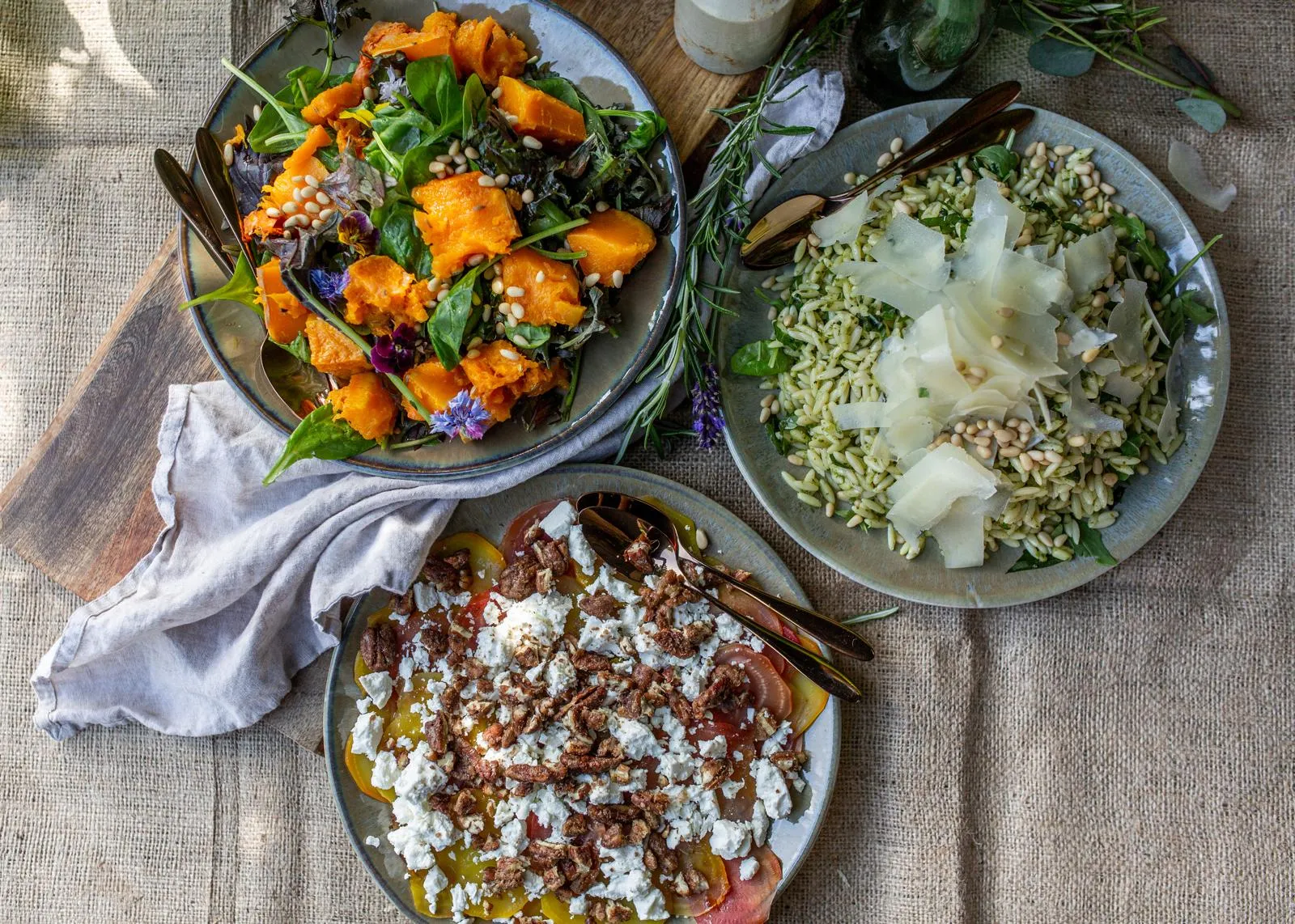 Roast pumpkin salad, pesto orzo with parmesan, and beetroot with feta and candied pecans on a linen table